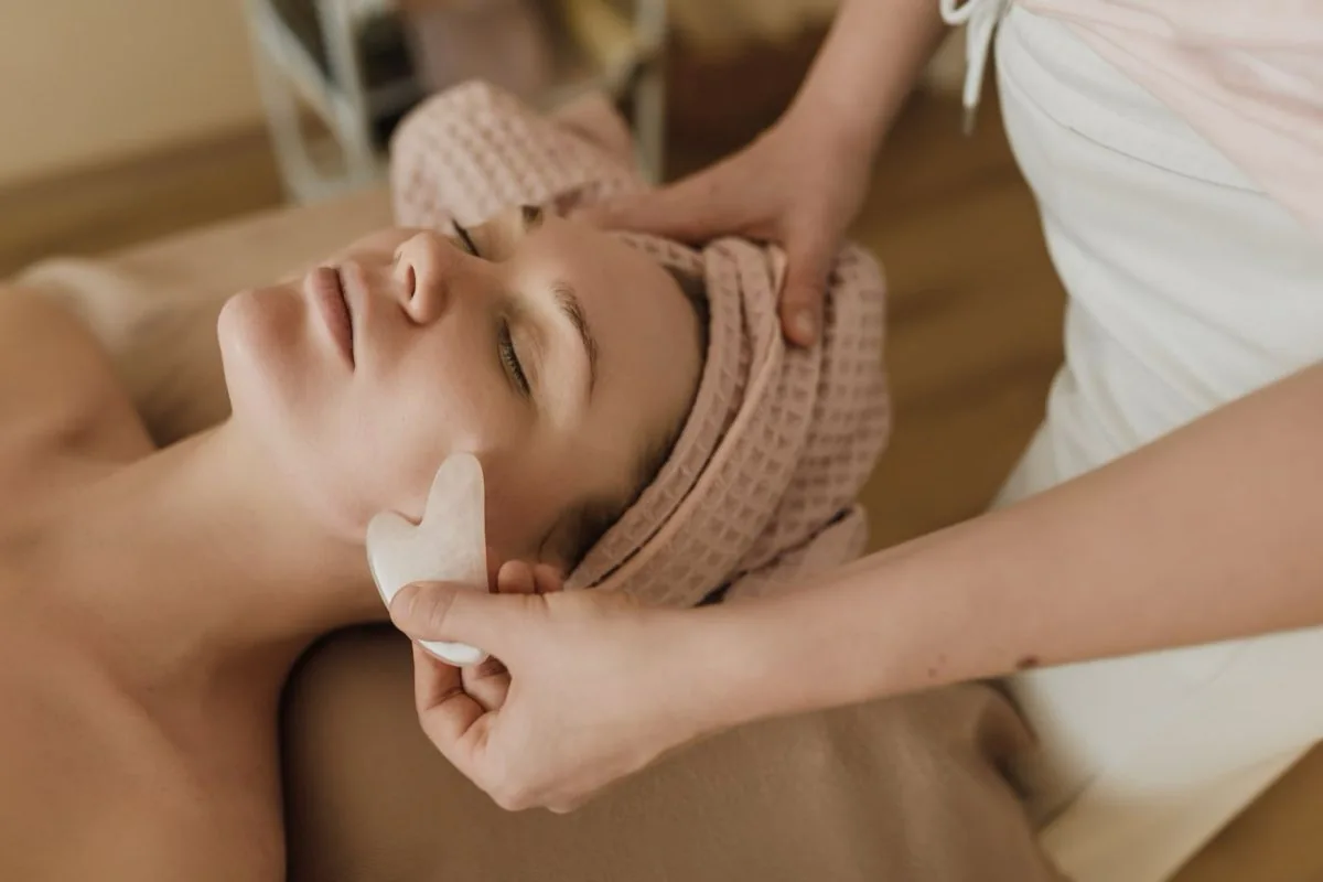 A practitioner using a gua sha tool during a facial treatment; illustrative photograph